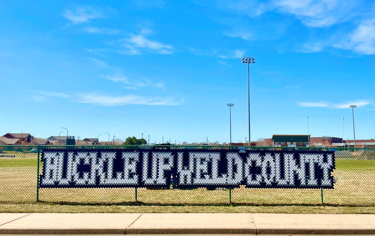 Bulldogs Buckle for Safety with Buckle Up Weld County message installed with fence cups in chain-link fence at University High School in Greeley.