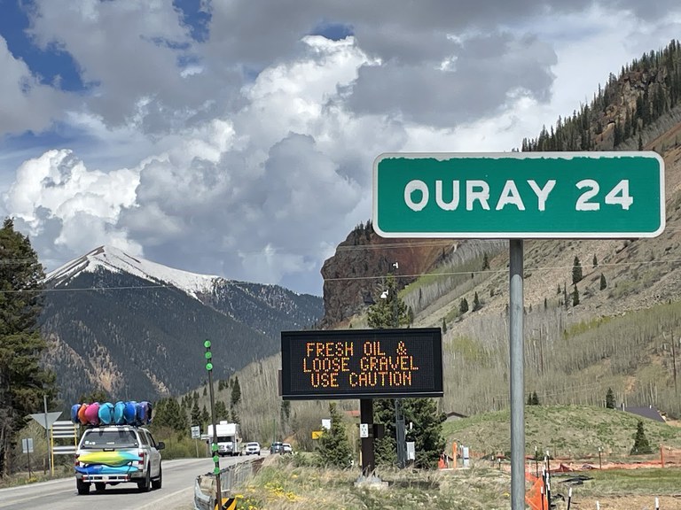 Chip Seal Operations on US 550 Red Mountain Pass between Silverton and Ouray. A Variable Message Sign (VMS) says Fresh Oil & Loose Gravel Use Caution