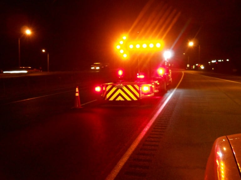 A CDOT attenuator vehicle on the roadside at night with a bright arrow sign indicating a crash or roadwork ahead.