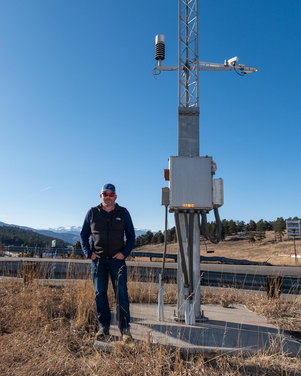 CDOT meteorologist Mike Chapman stands next to a CDOT weather station at the I-70 & Genesee exit