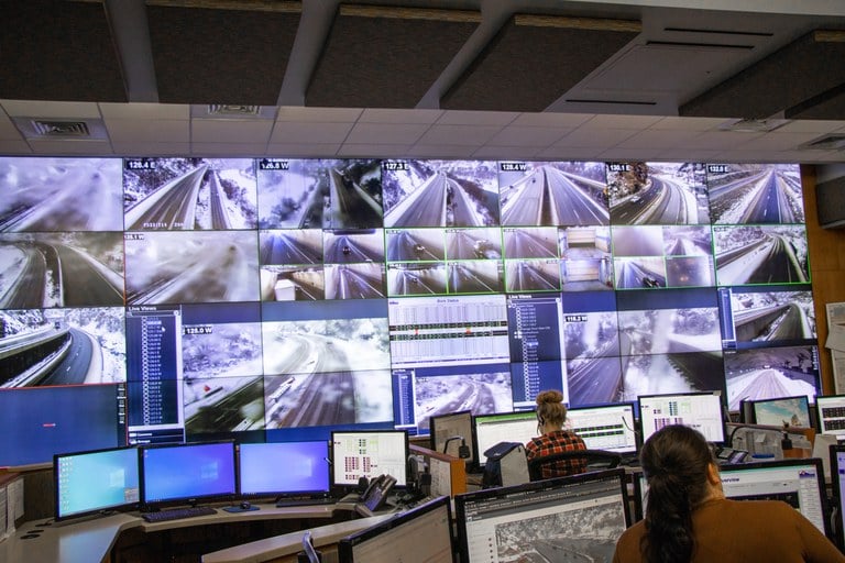 Two people watch over several screens showing road conditions