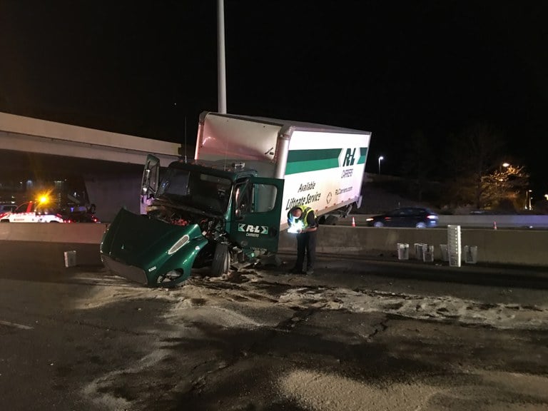 Law enforcement officer inspects a semi-truck that has gone over the median barrier