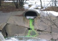 A bright green fluid leaving a culvert outlet and entering a waterway