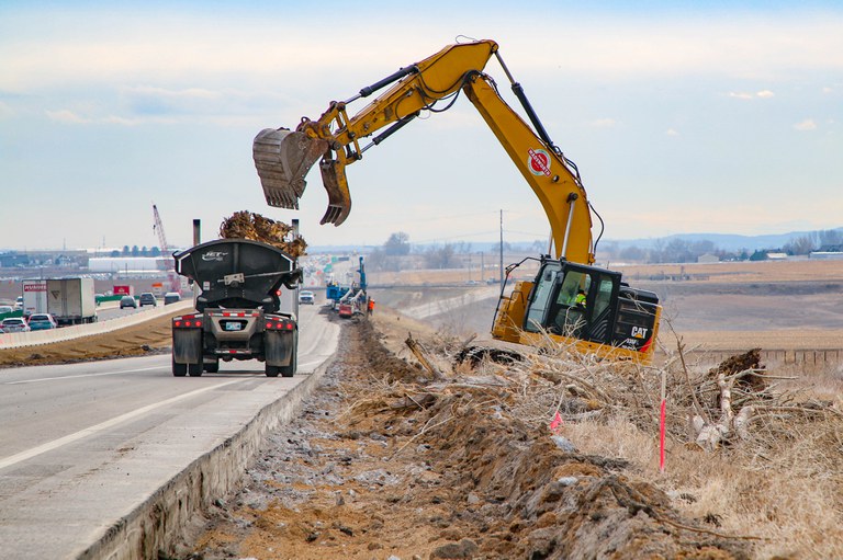 CAT vehicle unloading construction materials into a large truck bed on I-25 North.