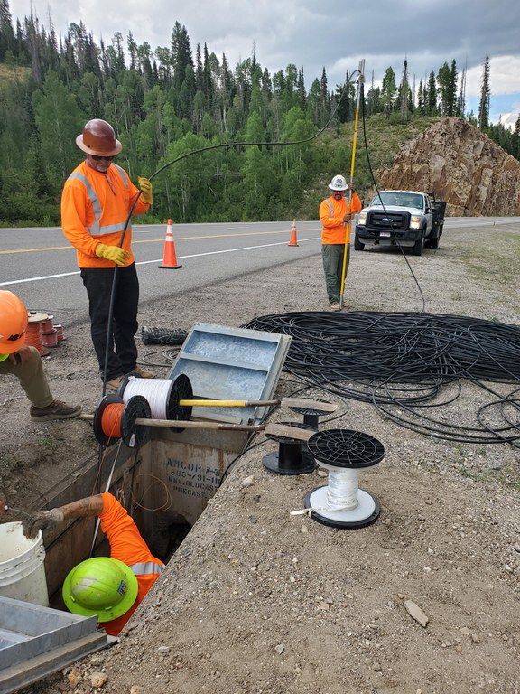 An installation crew pulls fiber optic cable through recently buried conduit
