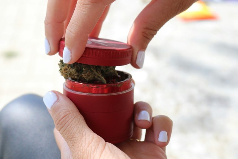 Hands loading weed into a fire engine red grinder.