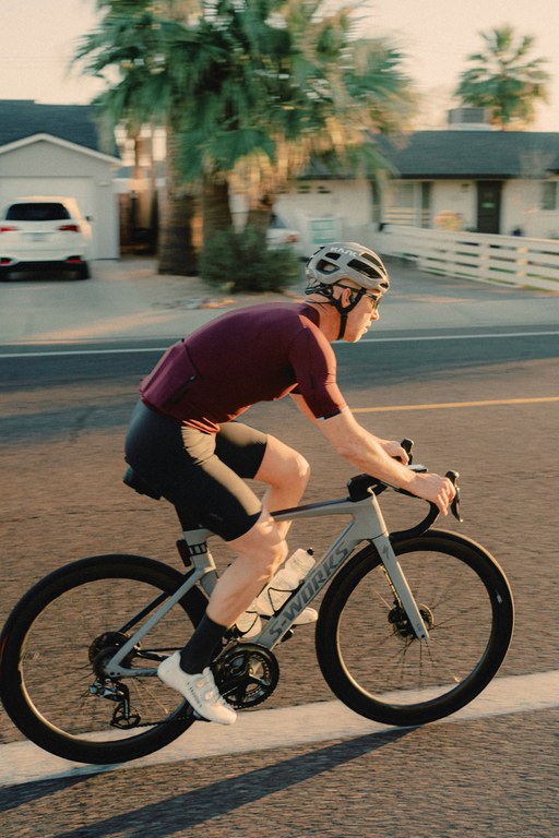 Bicyclist on a neighborhood street wearing maroon shirt, black shorts and light grey helmet.