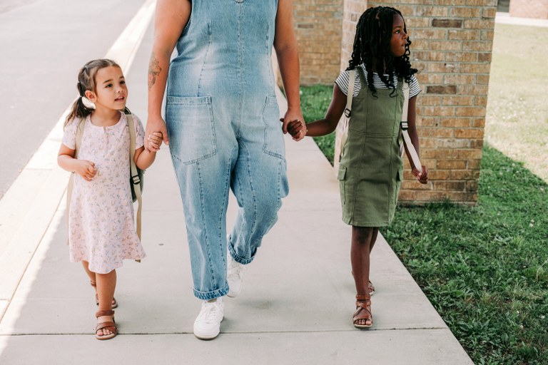 Two young girls holding an adult woman's hands and walking on a sidewalk.