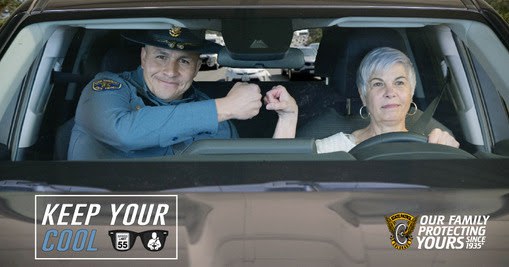 A police officer and older woman bumping fists in the front seats of a vehicle.