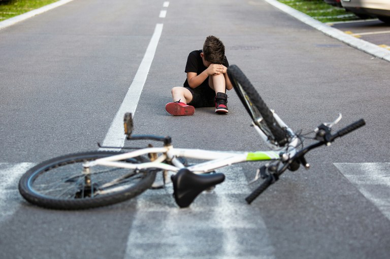 Young child holding his knee and sitting in an empty street. A white bicycle is fallen over on the ground in front of him.