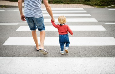 A man holding his young son's hand as they use a crosswalk.