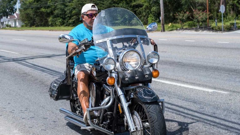 A man riding a motorcycle on a paved road without a helmet on.