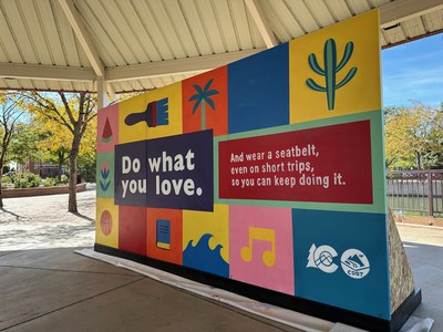 Colorful mural with painting of watermelon, basketball, music note, ocean waves, trees, flowers and pets. Text on the mural reads, "Do what you love. And wear a seatbelt, even on short trips, so you can keep doing it."