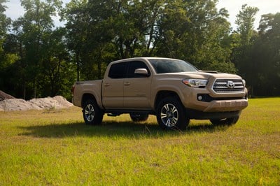 Tan pickup truck parked in a grass field with tall trees in the background.