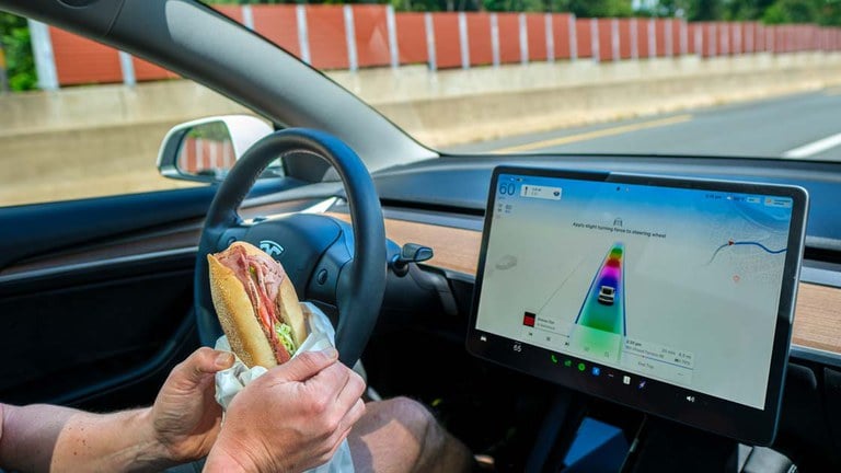 A person holding a sandwich with both while using partial automation behind the wheel of a Tesla.