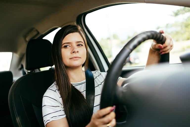 Teen driver with long hair and white shirt gripping the steering wheel of a vehicle.