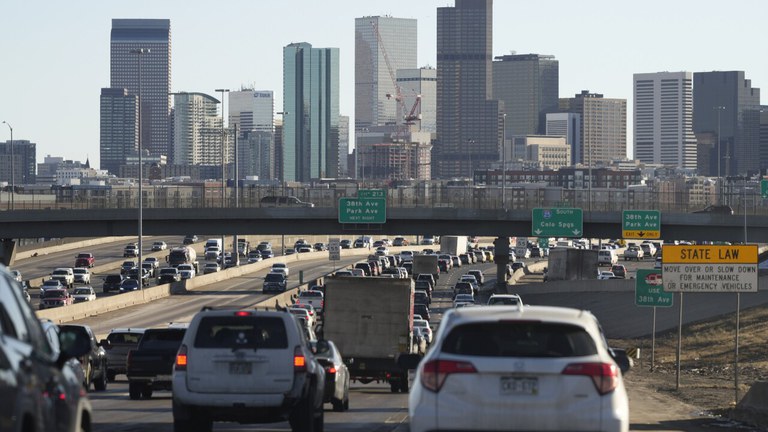 Heavy traffic on I-25 near downtown Denver with the city skyline in the distance. 