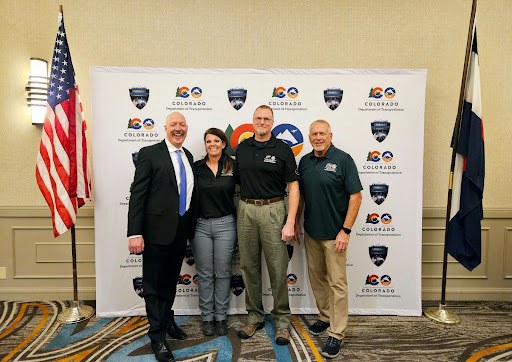 Drug Recognition Expert graduates standing in front of a white CDOT backdrop with the American flag and Colorado flag on either side.