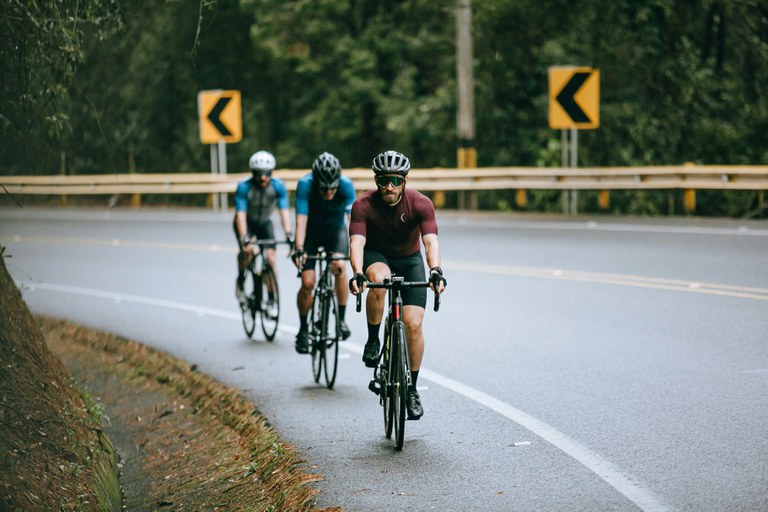 Three bicyclists wearing dark clothing and helmets on a curvy mountain road.