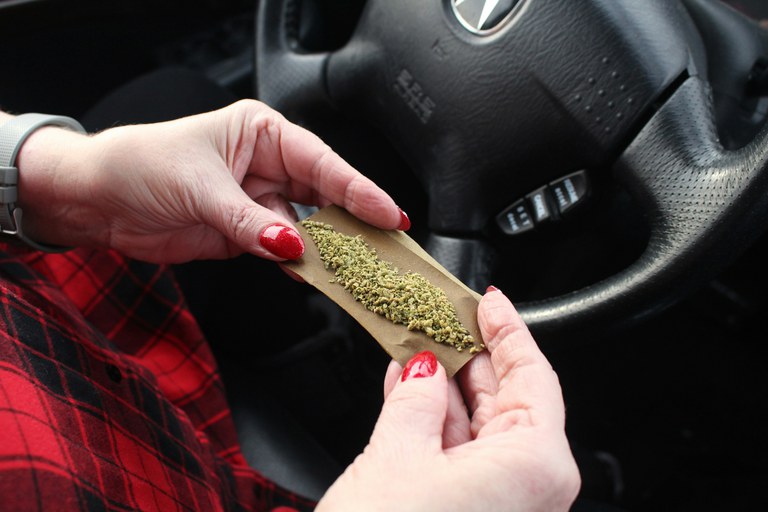 Person rolling a cannabis joint in the driver’s seat of a vehicle.