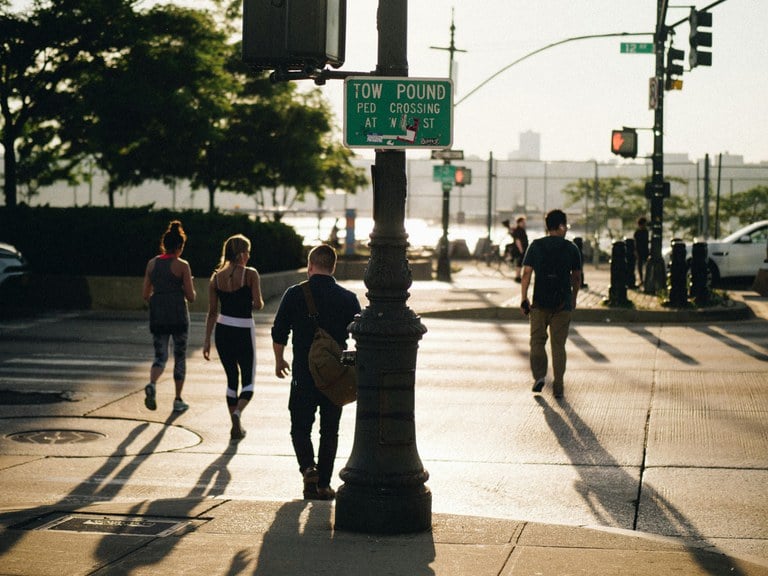 Pedestrians using a crosswalk on a city street with cars stopped at the red light.