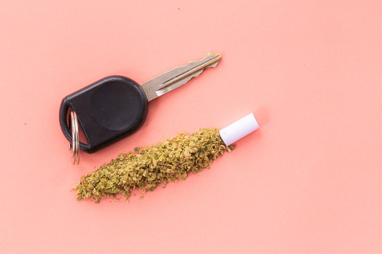 A car key next to an unrolled joint of cannabis, background is solid pink. 